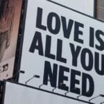 Large city billboard reads 'Love Is All You Need' in New York City street.