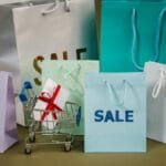 A mix of colorful shopping bags and a small cart displaying a discount gift.