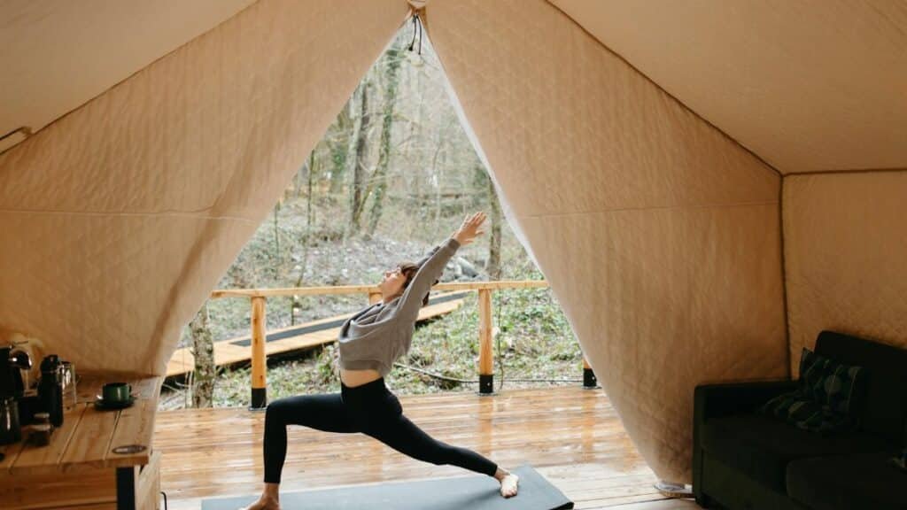 Person practicing yoga inside a cozy tent with a view of nature, embodying tranquility and fitness.