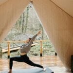 Person practicing yoga inside a cozy tent with a view of nature, embodying tranquility and fitness.