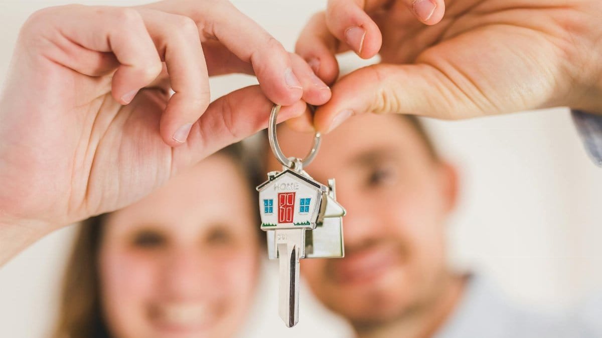 A smiling couple holds a house-shaped key, symbolizing their new home purchase.