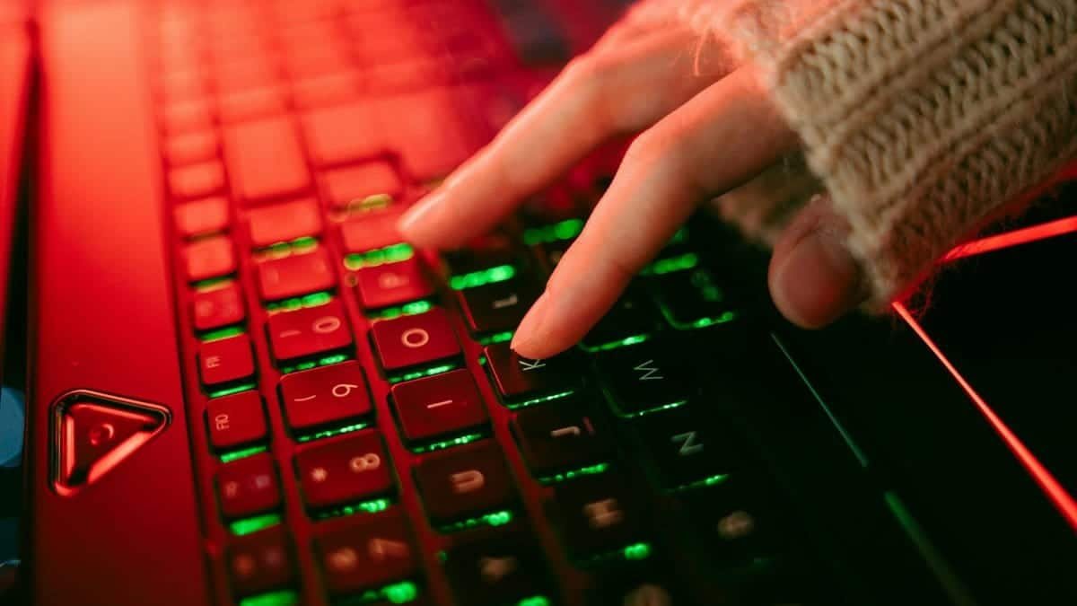 A hand typing on a backlit keyboard in a dark ambiance, highlighting vibrant key illumination.