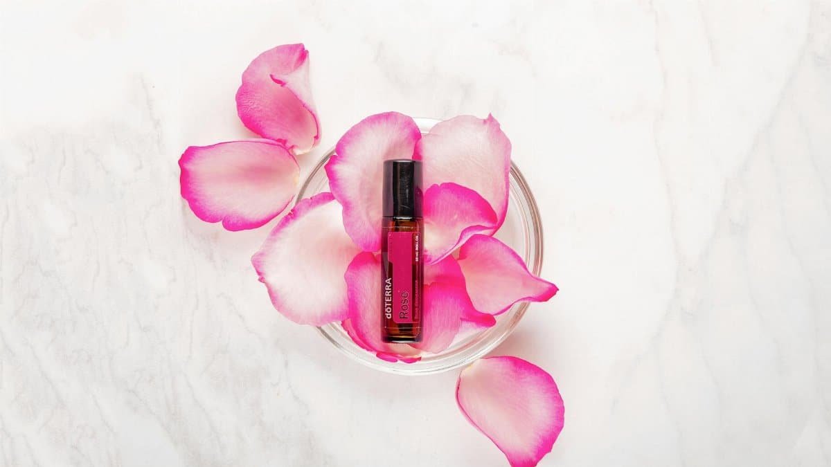Rose essential oil bottle surrounded by pink rose petals on a marble surface.
