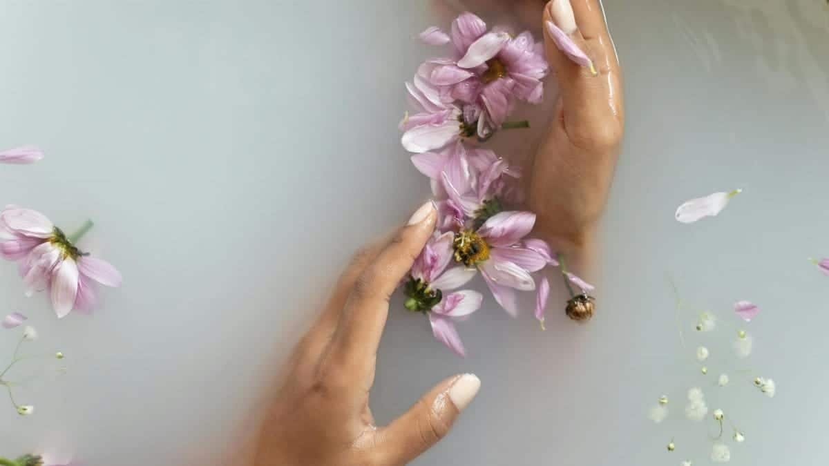 Gentle hands with pink flowers in a soothing bath, representing tranquility and skin care.