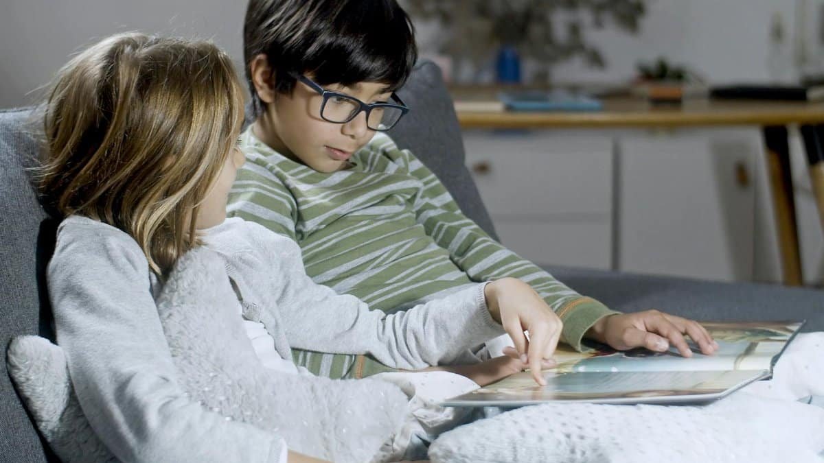 Two children enjoy reading a book together on a cozy sofa at home, fostering a love for stories.