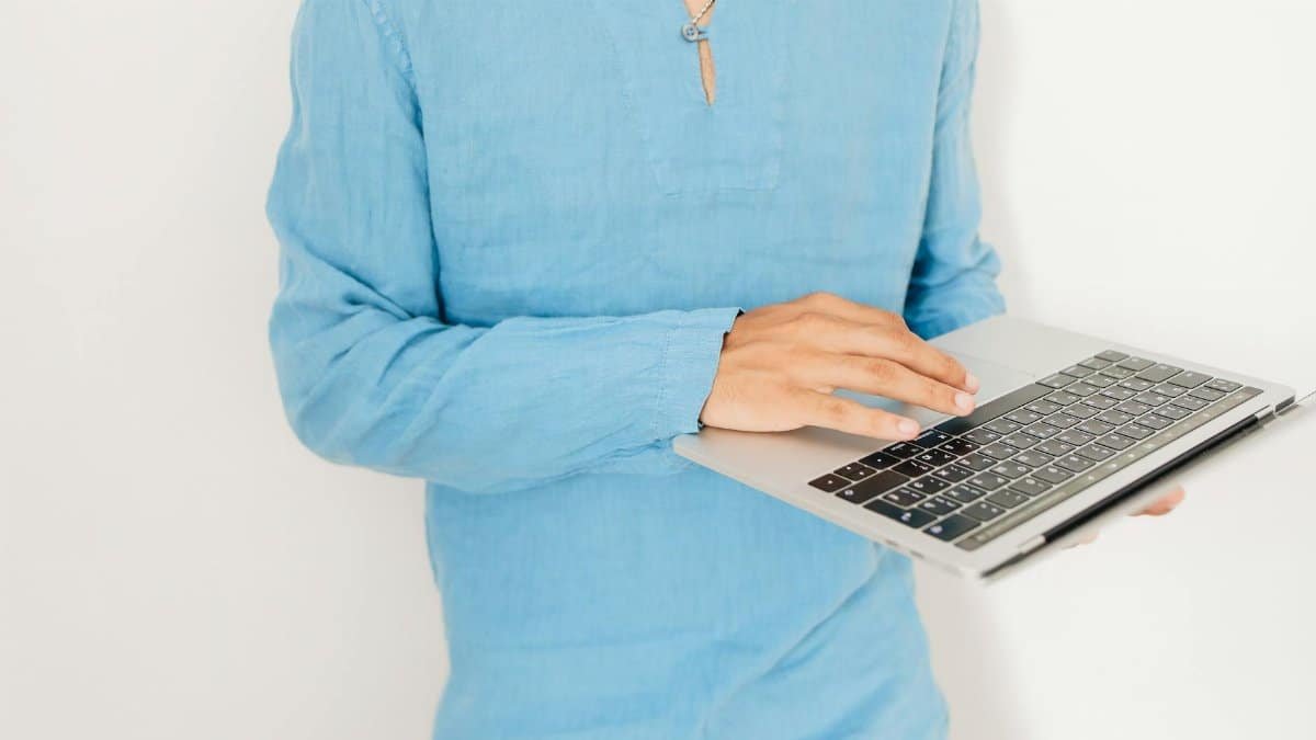 Close-up of a person using a laptop, wearing a casual blue shirt against a plain background.