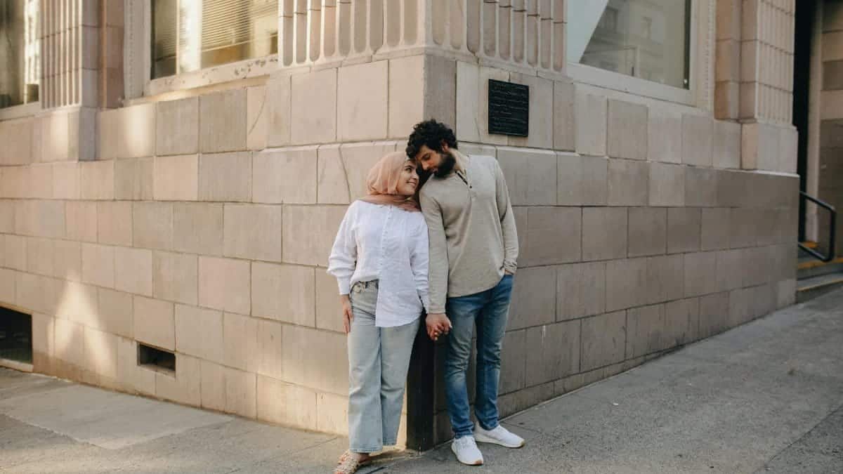 A loving couple stands and holds hands outside an urban building, showcasing a tender moment.