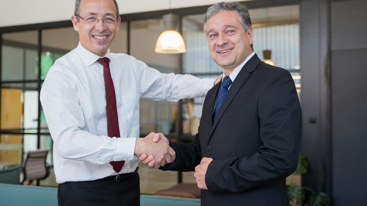 Two businessmen shaking hands in a modern office, symbolizing a successful agreement or partnership.