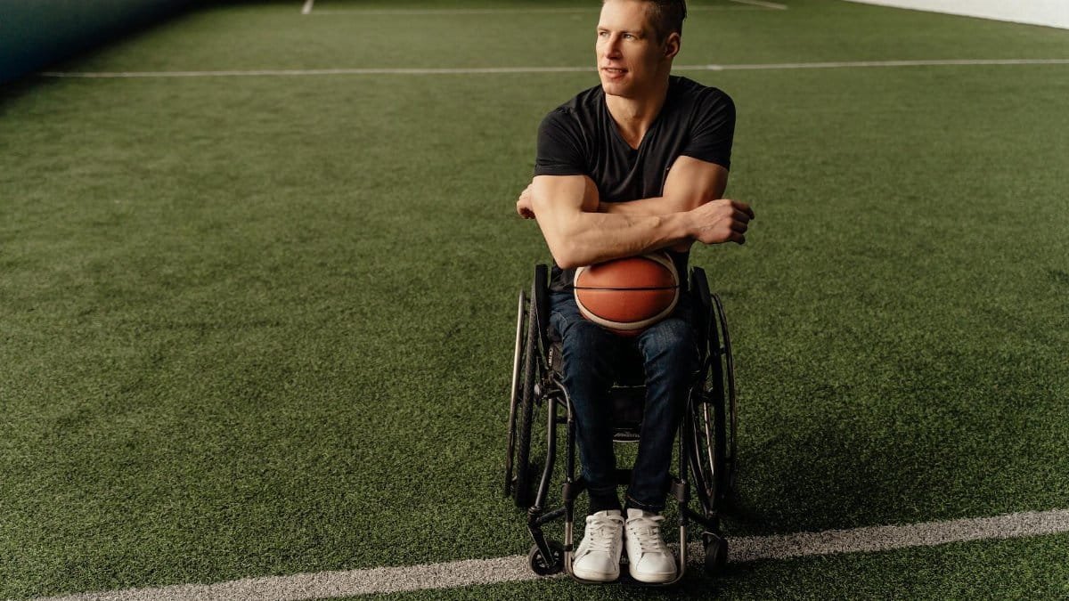 Adult man in wheelchair holding basketball on the field symbolizing adaptive sports and determination.