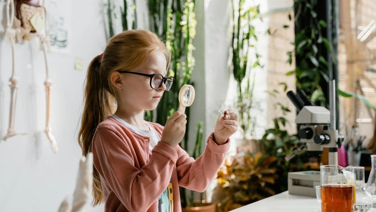 A young girl uses a magnifying glass to study samples in a vibrant indoor lab environment.