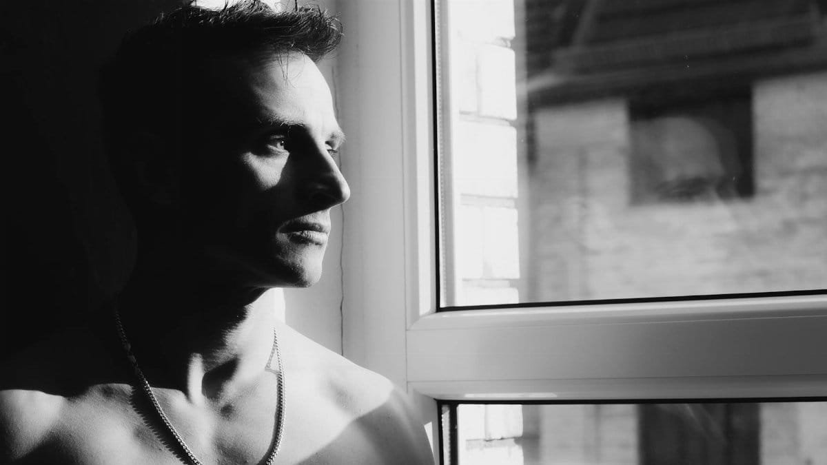 Expressive black and white portrait of a man looking out a window, capturing deep emotion and thought.