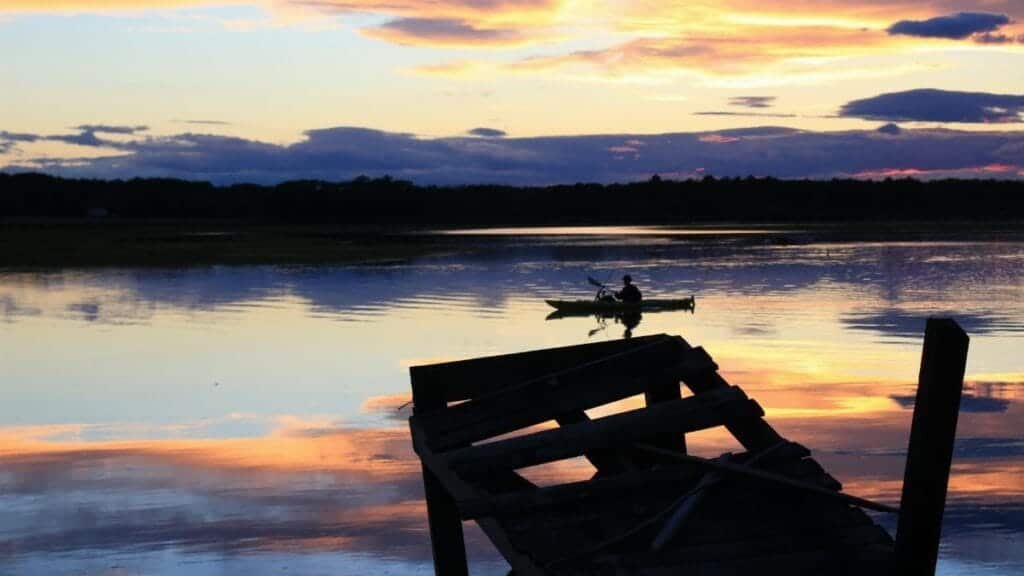 Serene lake view with silhouetted canoeist at sunset in Scarborough, Maine.