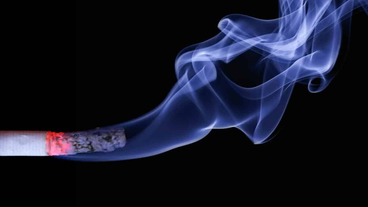 Detailed close-up of a cigarette with glowing ember and swirling smoke on a black background.