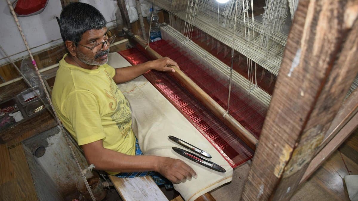 Elderly man weaving silk fabric using traditional methods in Varanasi workshop.