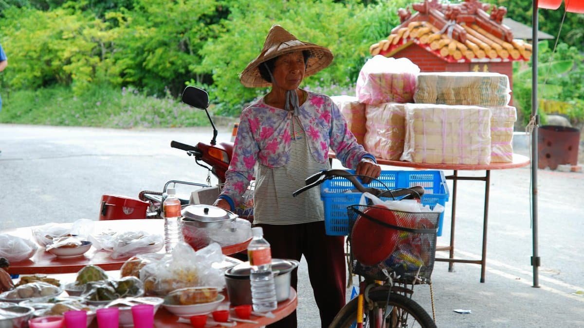 An elderly vendor with a bicycle at an outdoor food market, showcasing local goods.