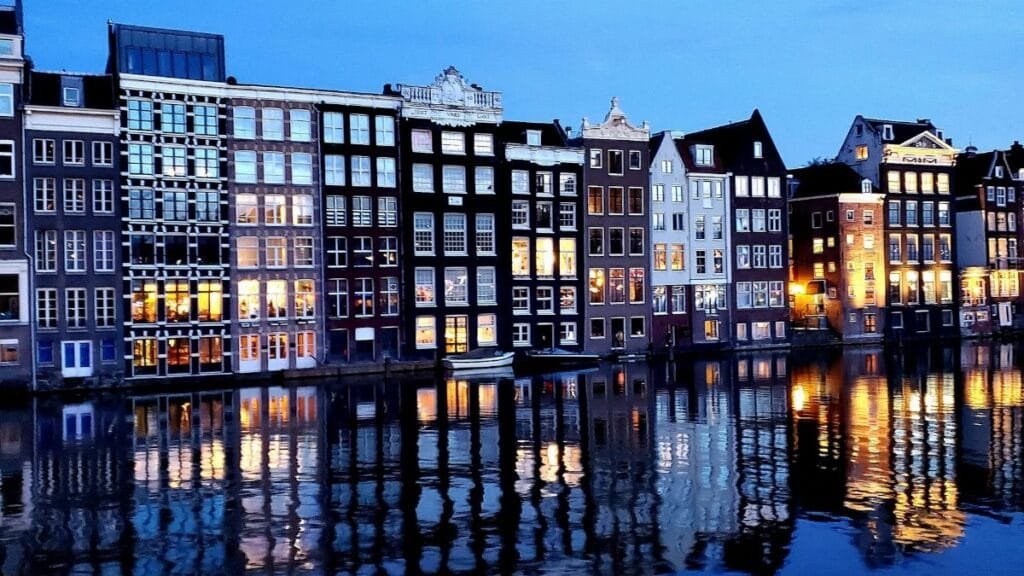 View of Amsterdam's iconic canal houses reflecting in the evening waters, showcasing classic Dutch architecture.