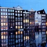 View of Amsterdam's iconic canal houses reflecting in the evening waters, showcasing classic Dutch architecture.