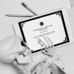 Black and white image of skeleton hand holding tablet with 'Certificate of Death' showing overworked.