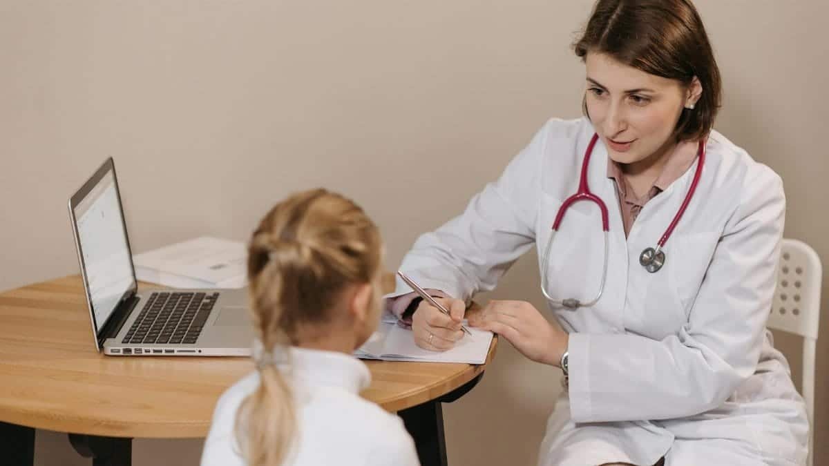 A female doctor listens attentively to a young girl during a medical consultation in an office setting.