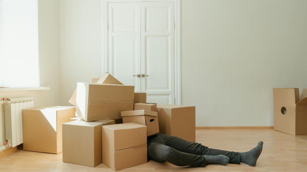 Person on floor surrounded by cardboard boxes during moving; concept of stress and relocation.