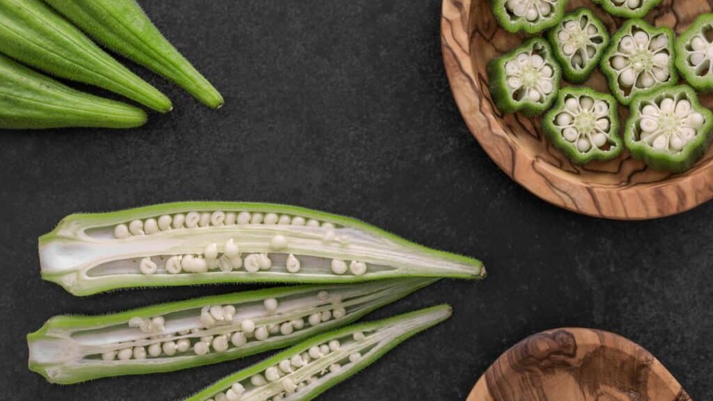 Close-up of fresh okra pods and slices on a dark background.