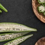 Close-up of fresh okra pods and slices on a dark background.