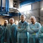 Group of diverse workers wearing blue protective clothing in an industrial setting.