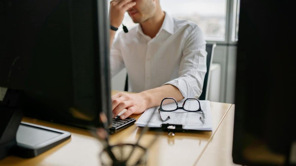 Man at office desk holding head in frustration, signifying stress at work.