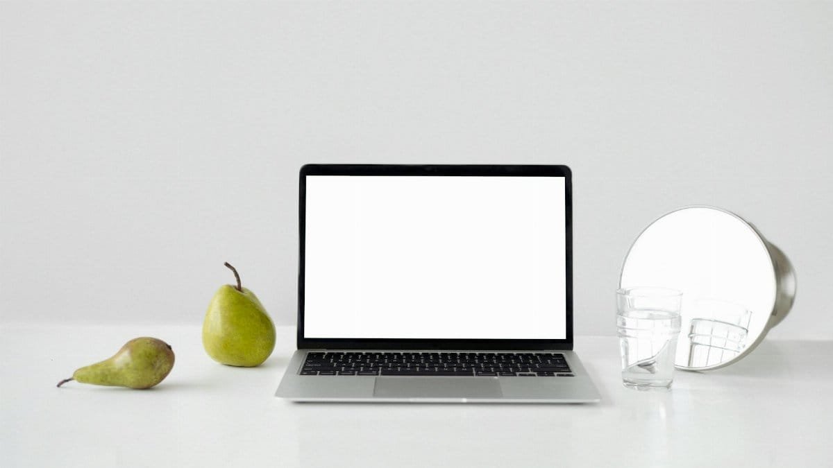 A minimalist desk setup featuring a laptop, pears, and a mirror for a modern look.