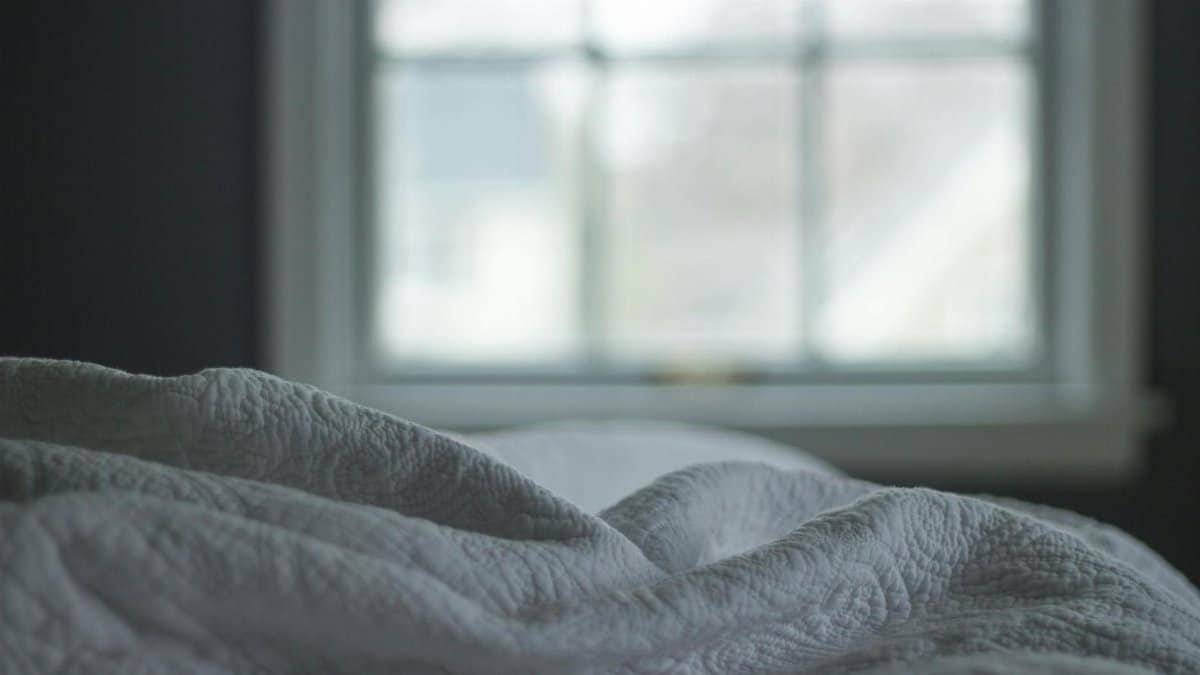 A tranquil bedroom view with a quilted blanket by the window softly lit by morning light, ideal for relaxation themes.