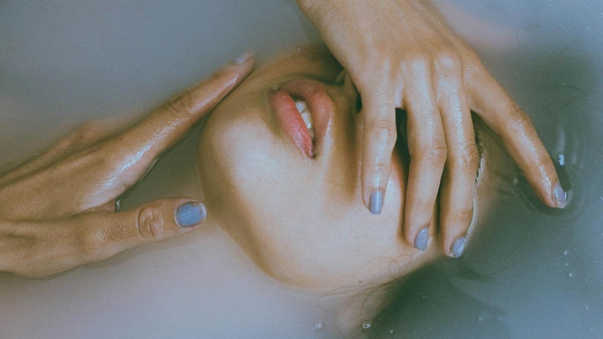 Creative close-up of a woman's face with hands emerging from water, evoking mystery and elegance.