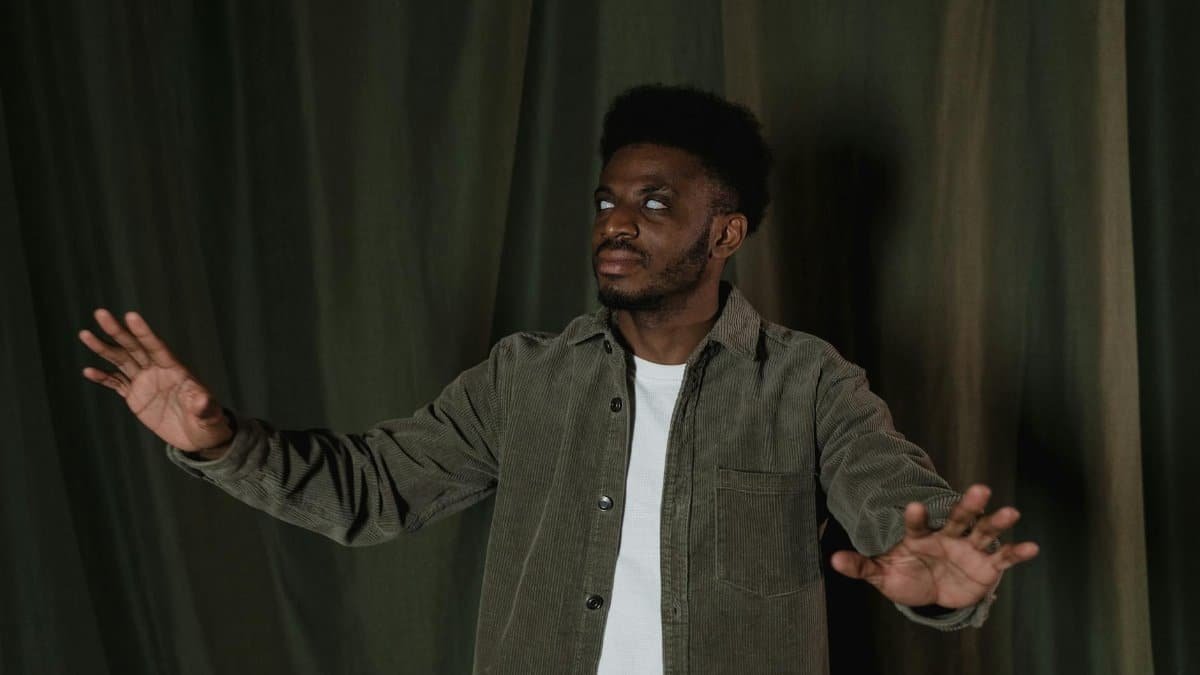 African man with visual impairment navigating with his hands in a dimly lit room.
