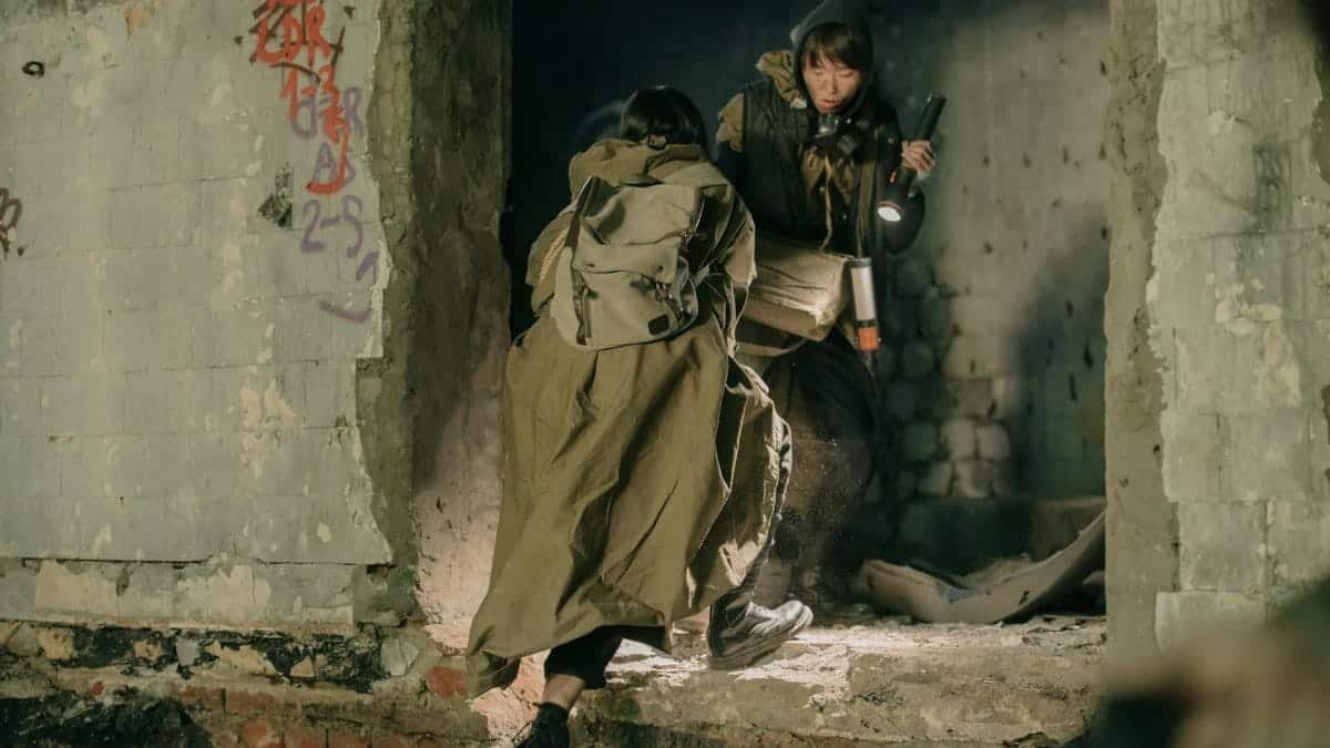 Two people exploring and navigating through abandoned ruins with a flashlight, amidst debris and decay.