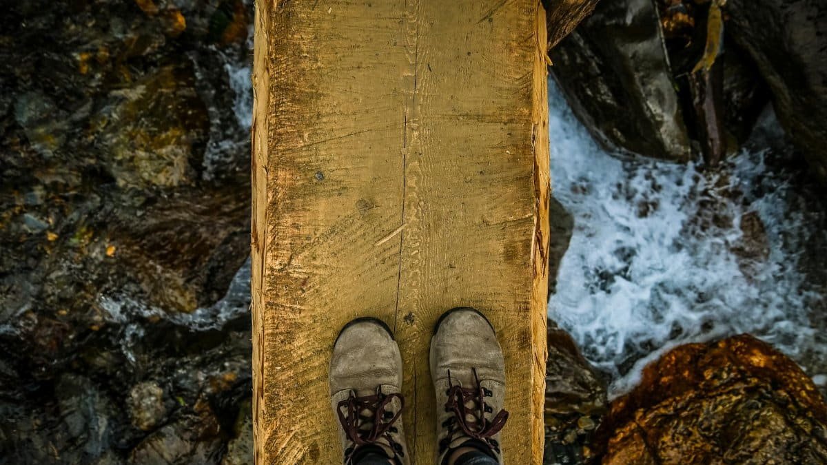 View of a person standing on a narrow wooden bridge over rushing river rapids.