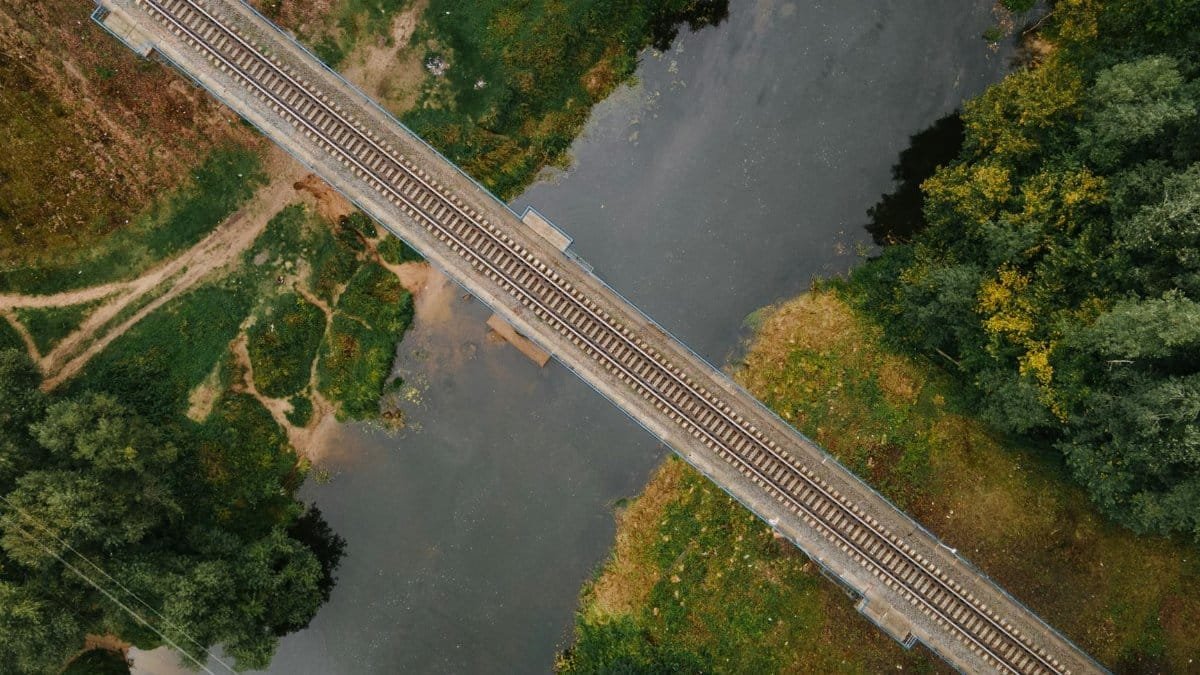 An aerial shot capturing a railway bridge crossing over a river in a lush, rural setting.