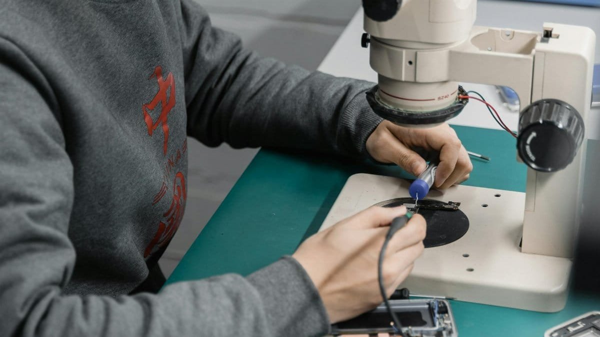 A technician examines a circuit board under a microscope for electronic repair.