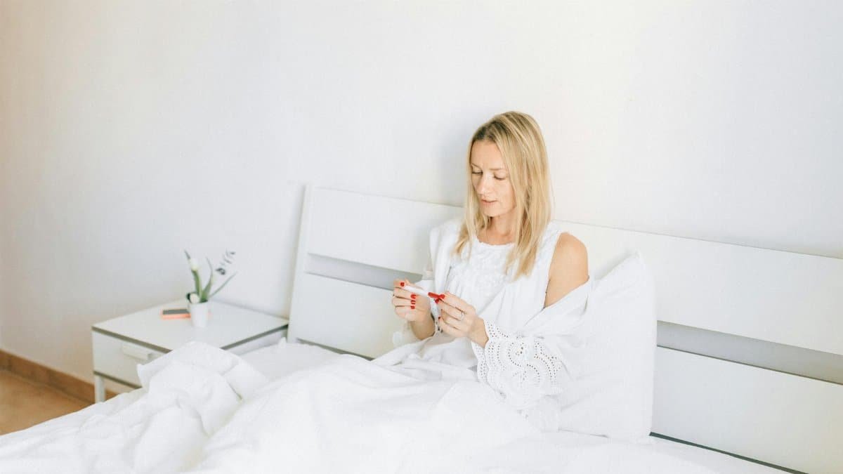 Woman sitting in bed examining a pregnancy test, conveying anticipation and hope.