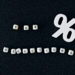 Conceptual image of tax deductions with alphabet blocks and percent symbol on black surface.