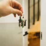 A hand holding a house key indoors signifies new ownership or leasing in real estate.