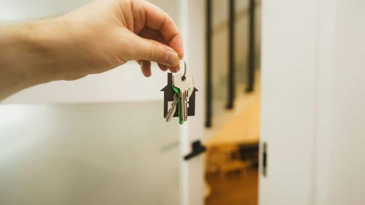 A hand holding a house key indoors signifies new ownership or leasing in real estate.