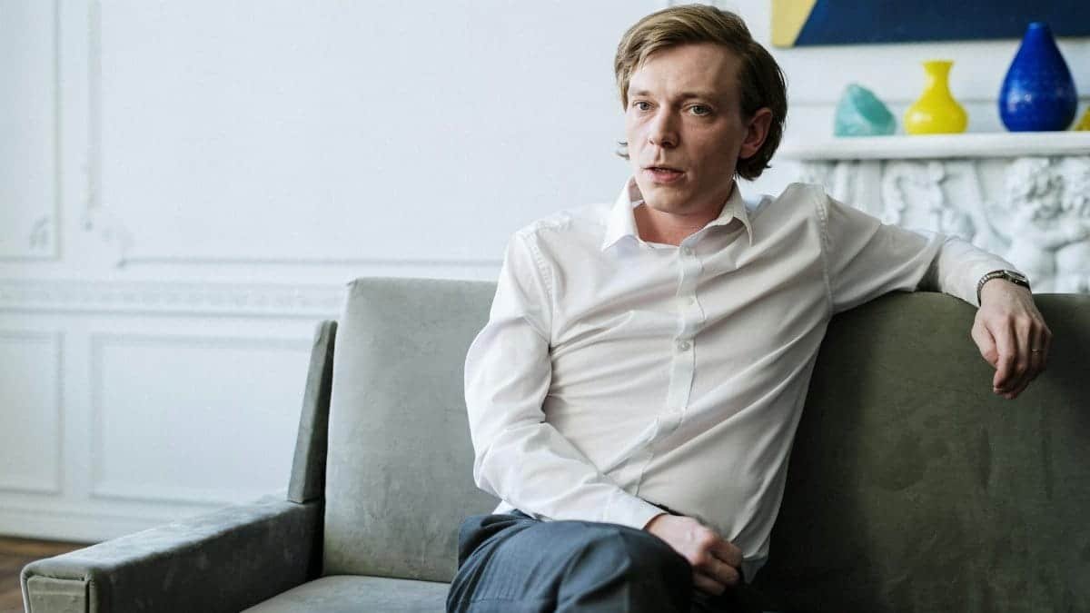 Confident man in white shirt sitting on sofa, representing consulting or therapy session indoors.