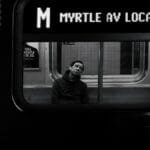 Black and white photo capturing a commuter in deep thought on the NYC Subway.