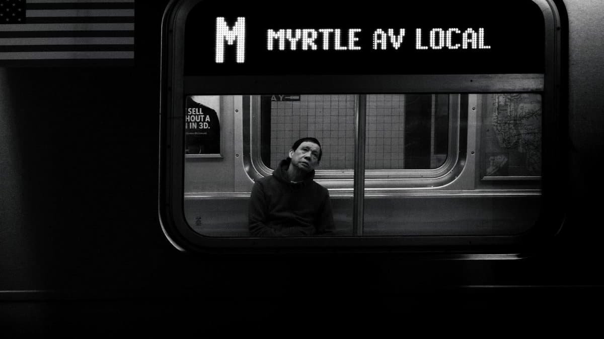 Black and white photo capturing a commuter in deep thought on the NYC Subway.
