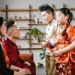 Asian family exchanging red envelopes during Lunar New Year celebration indoors.