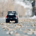 Miniature toy car on an autumn road with scattered leaves, showcasing detail and seasonal charm.