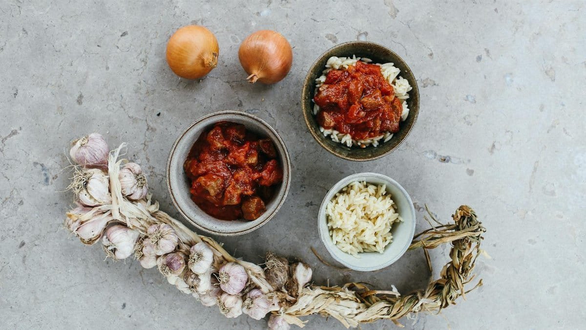 A savory chicken curry plated with rice, garnished with garlic and onions on a textured surface.
