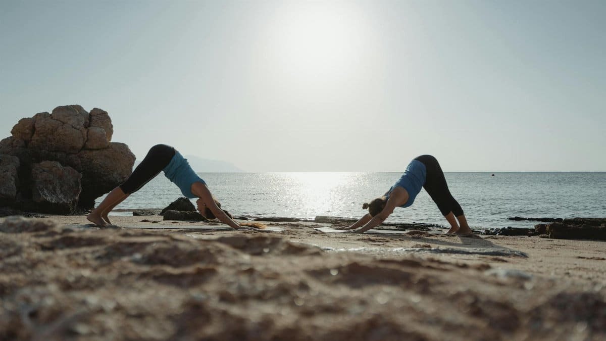 Two women practicing yoga at dawn on a serene beach with clear waters.
