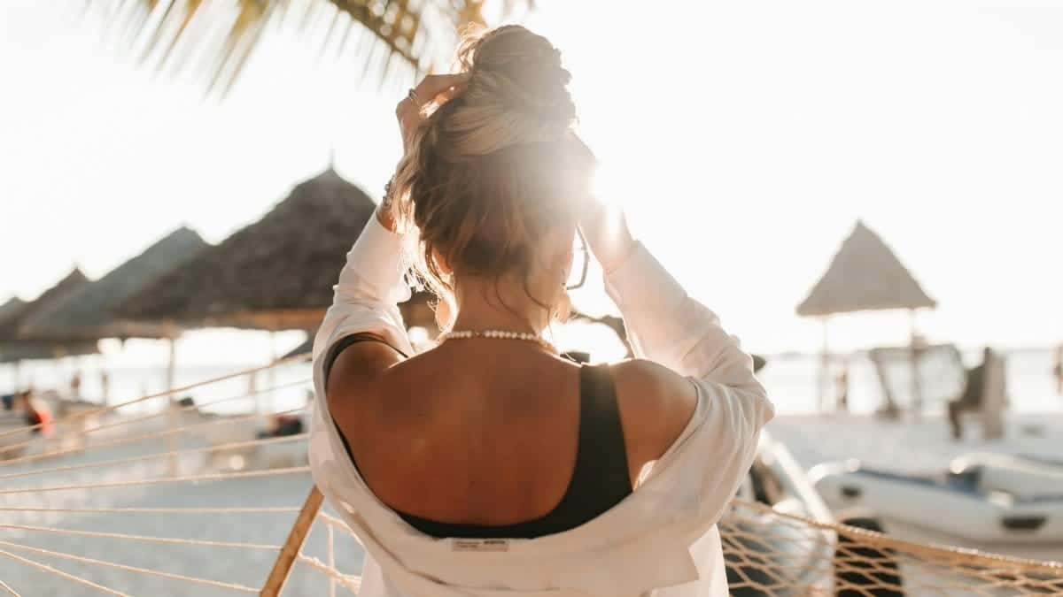 A woman stands on a sunny beach with a back view, dressed in a black top and white shirt.