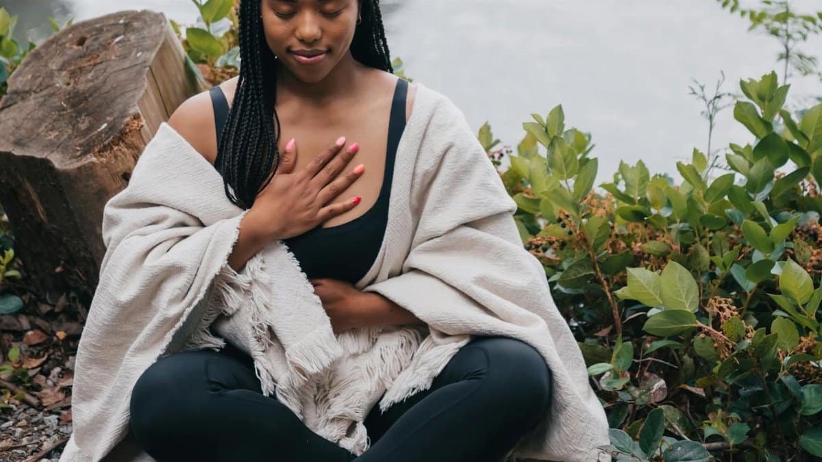 A woman practicing mindful meditation outdoors by the water, symbolizing wellness and relaxation.
