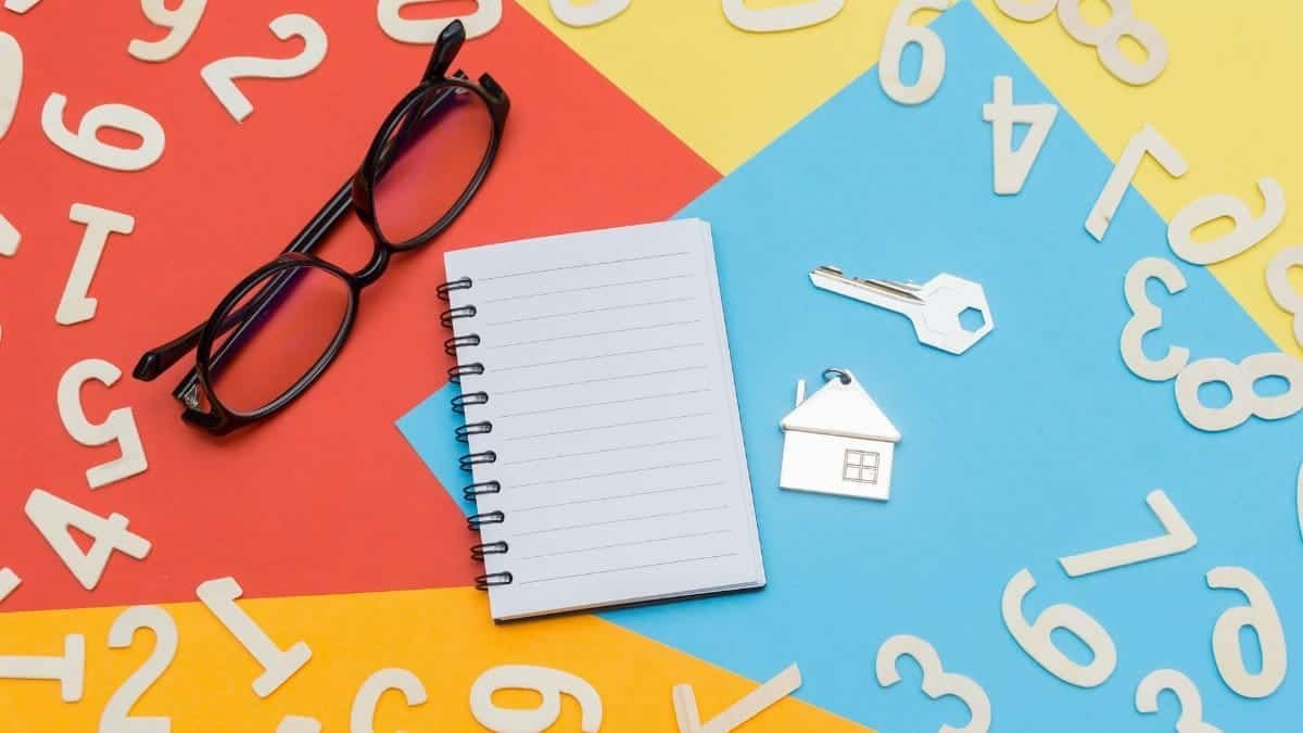 Flat lay of a colorful desktop featuring a notebook, eyeglasses, and house key with numbers scattered.